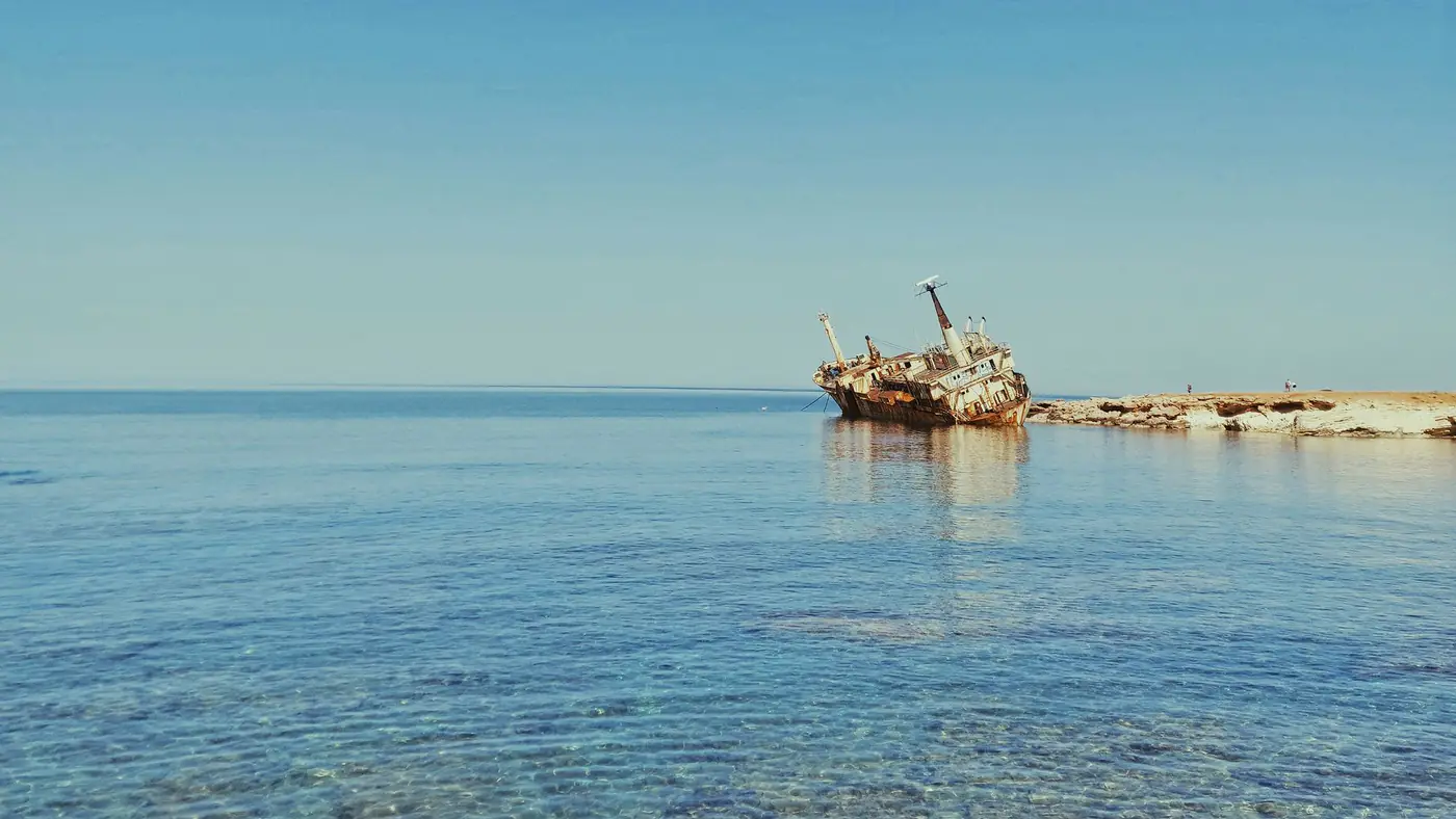 A scenic view of an abandoned shipwreck near the coast of Paphos, Cyprus, under a clear blue sky.