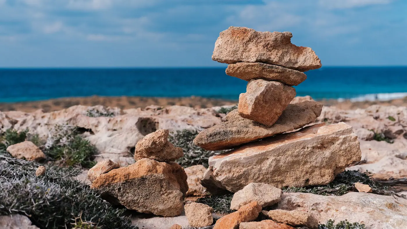 Serene view of balanced stones on rocky coast with blue sea and sky in Cyprus.