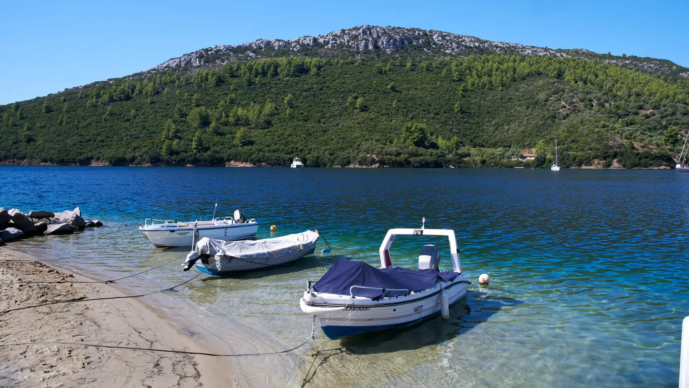 Peaceful scene of boats anchored on a serene Aegean beachfront with lush hills in Greece.