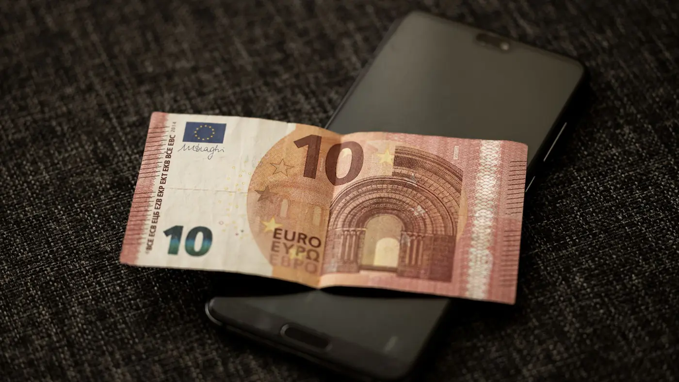 A close-up shot of a 10 euro banknote placed on a smartphone, highlighting currency and digital technology.