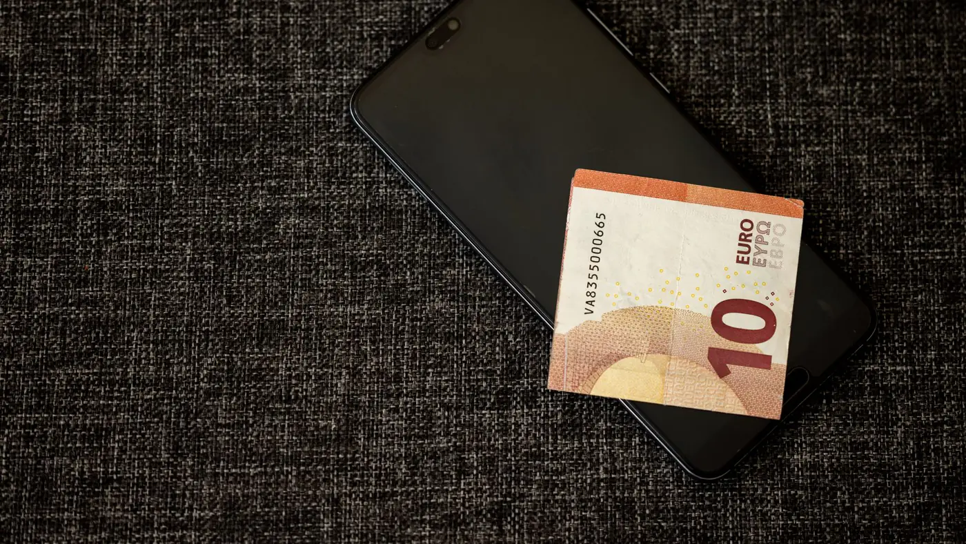 A 10 euro banknote placed on a smartphone on a textured dark fabric background.