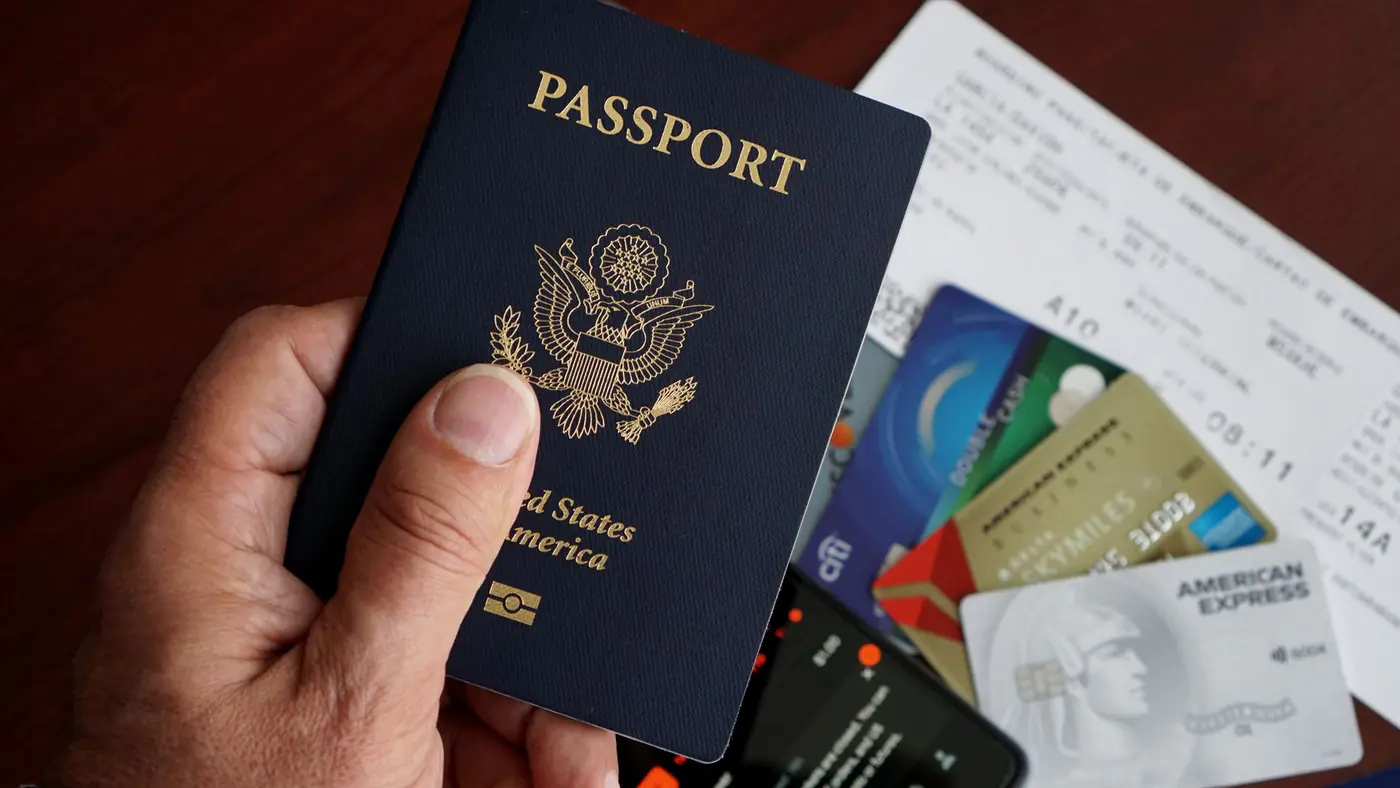 A close-up of a US passport with credit cards, tickets, and a mobile phone on a table.