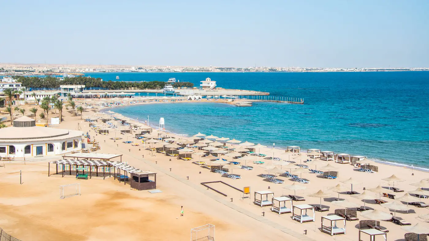 Aerial view of a serene beach resort with umbrellas, calm blue sea, and sandy shore.