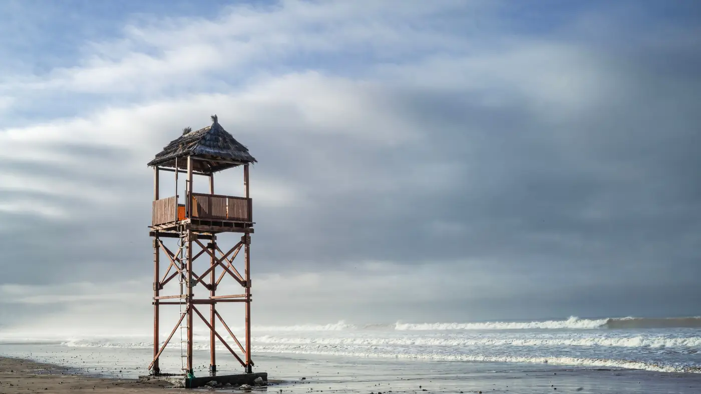 A solitary lifeguard tower stands on a deserted beach in Agadir, Morocco under a cloudy sky.