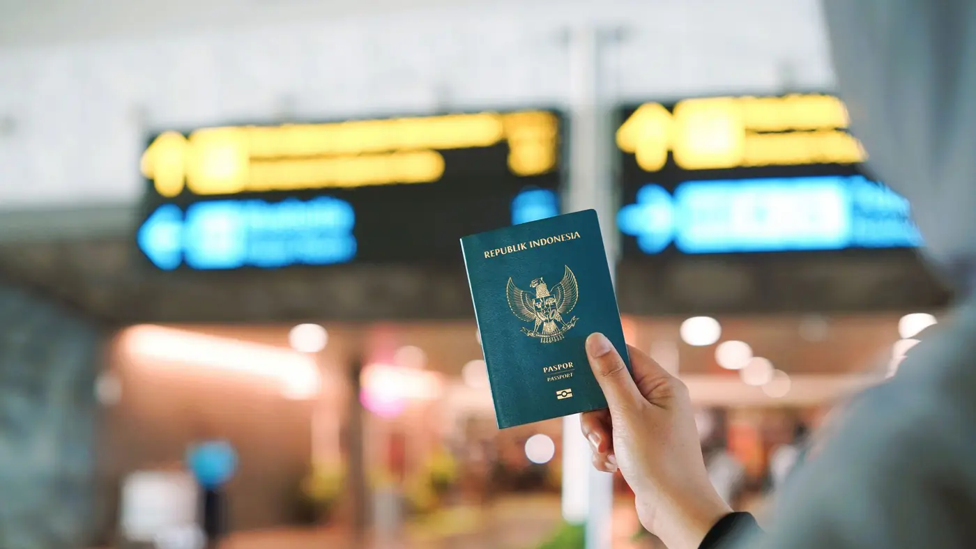 A person holding an Indonesian passport at a busy airport terminal in Yogyakarta, Indonesia.