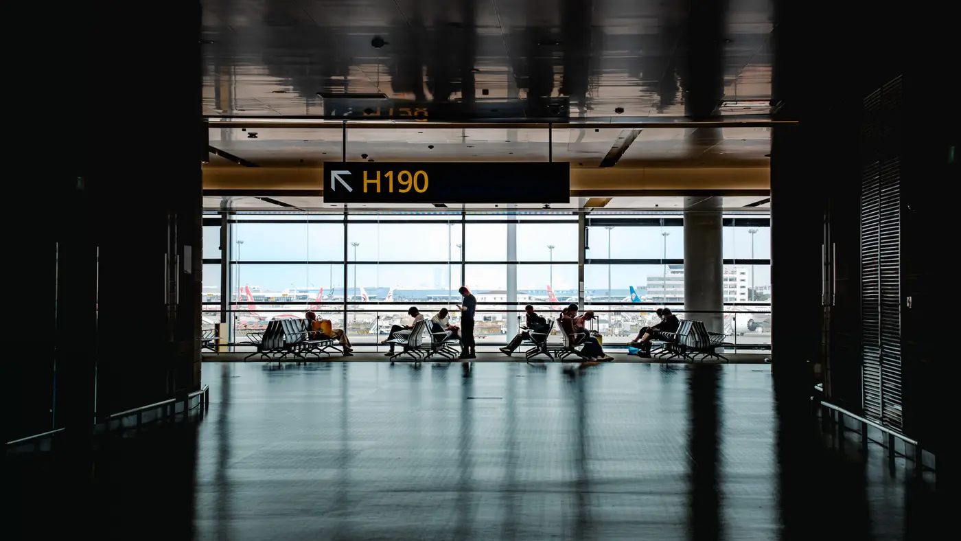 Silhouetted travelers waiting at Shanghai airport terminal gate H190 with cityscape view.