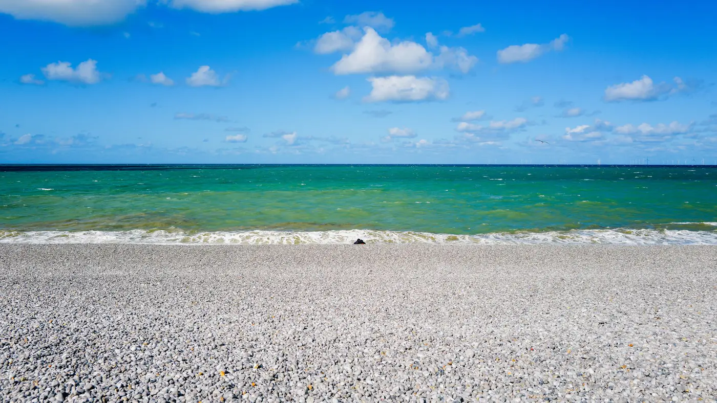 Serene pebble shoreline with clear blue skies and turquoise ocean waves, ideal for relaxation imagery.