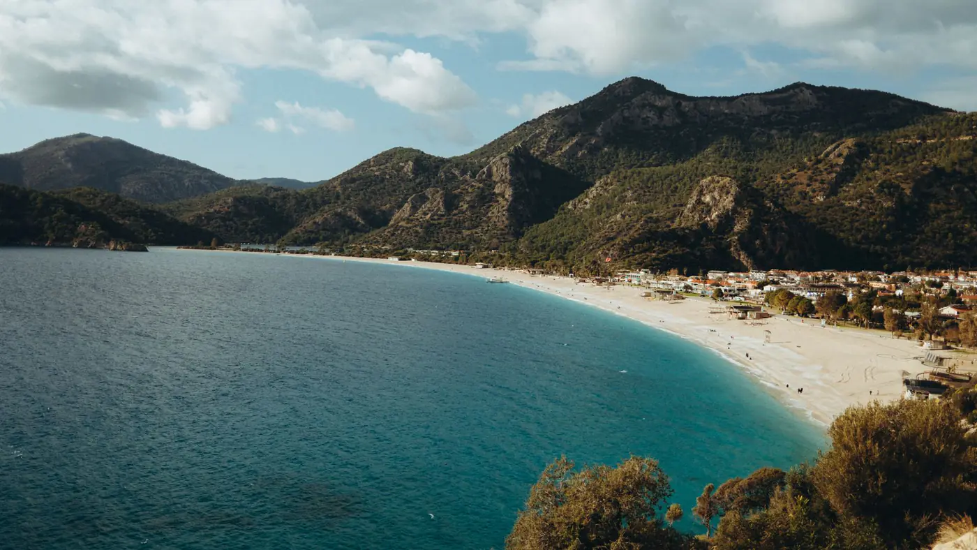 Stunning coastal view of Ölüdeniz beach with mountains and turquoise sea under a cloudy sky.