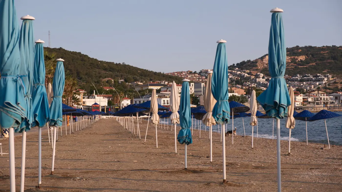 A scenic view of empty beach umbrellas along the Foça coast in İzmir, Türkiye at sunset.