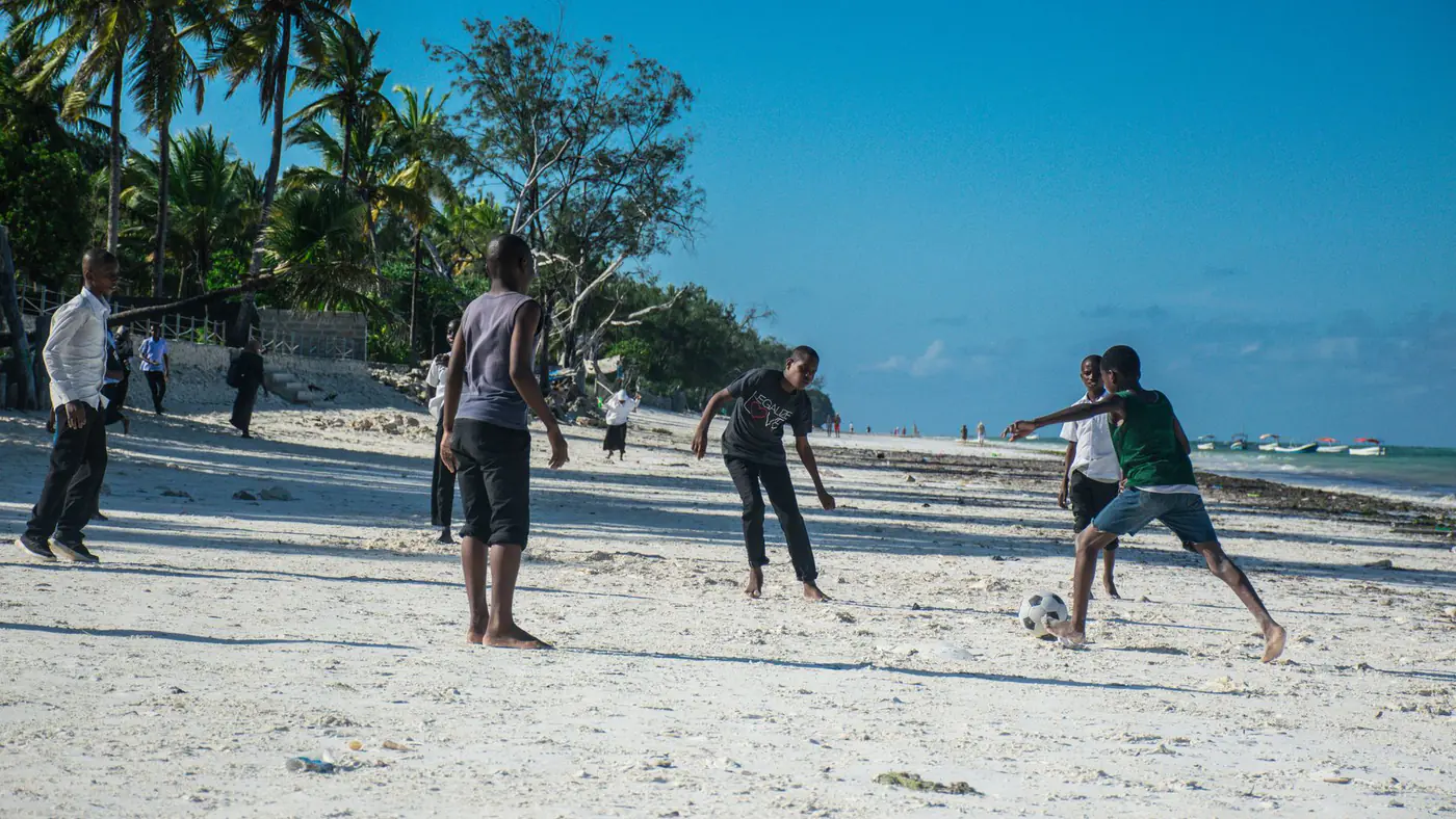 Group of boys enjoying a lively soccer game on a sunny Zanzibar beach.